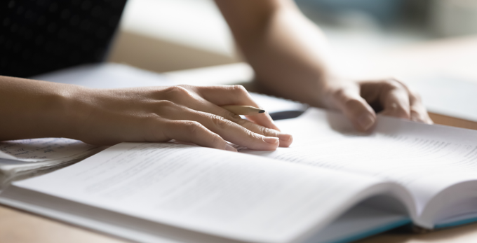 Female reading book and writing notes with a pencil on an office table, hands with pencil close up.