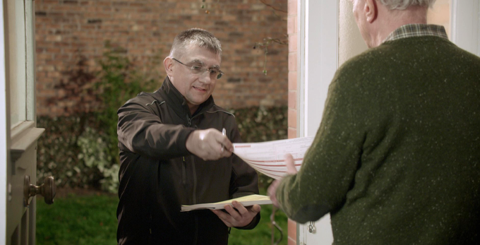 A contractor, standing in the front door way, handing a homeowner a written summary of electrical work undertaken.