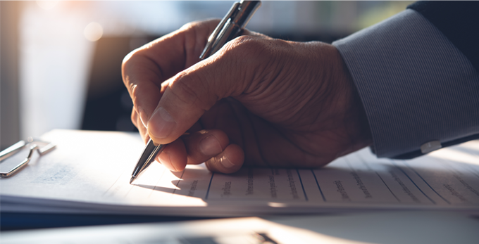 Businessman, reviewing and amending corporate document with ball point pen, and working on laptop computer on desk in modern office, close up