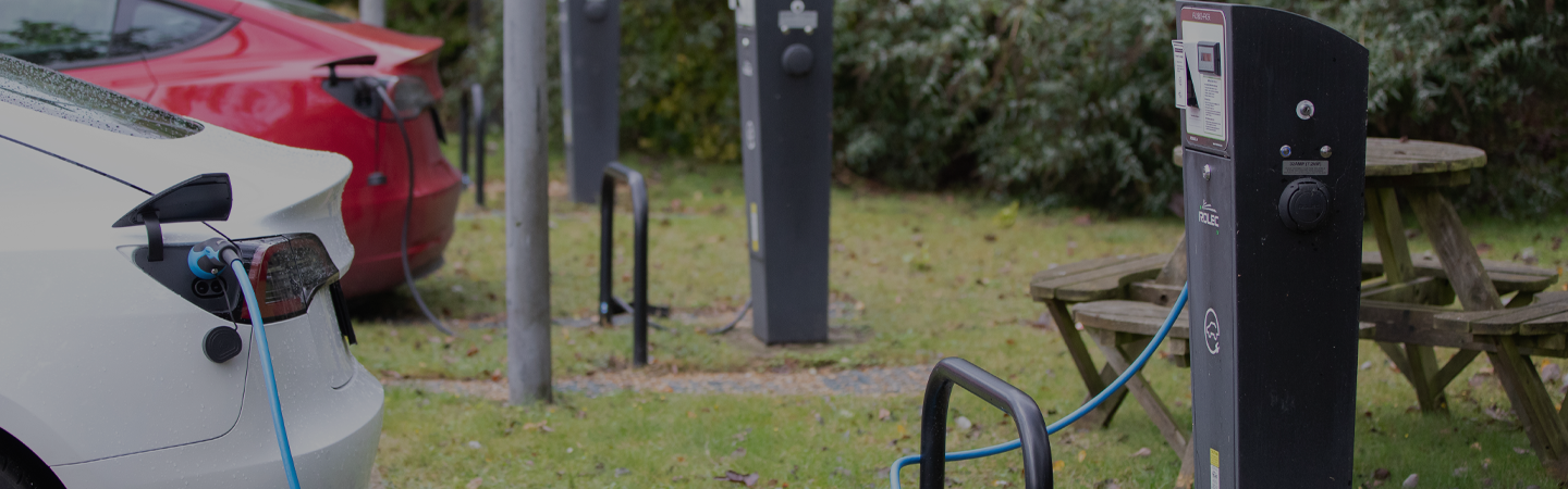 Red and white Tesla electric vehicles parked stationary, plugged into the charging station.