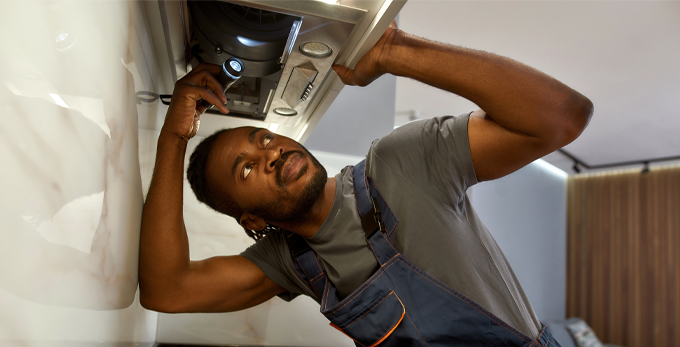 A contractor using a torch to inspect oven ventilation hood in a kitchen.