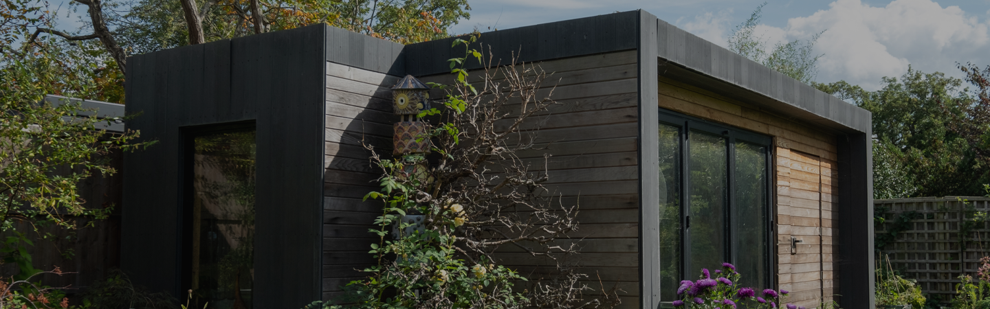 A modern, wooden cladded structure in a garden in the summer months.