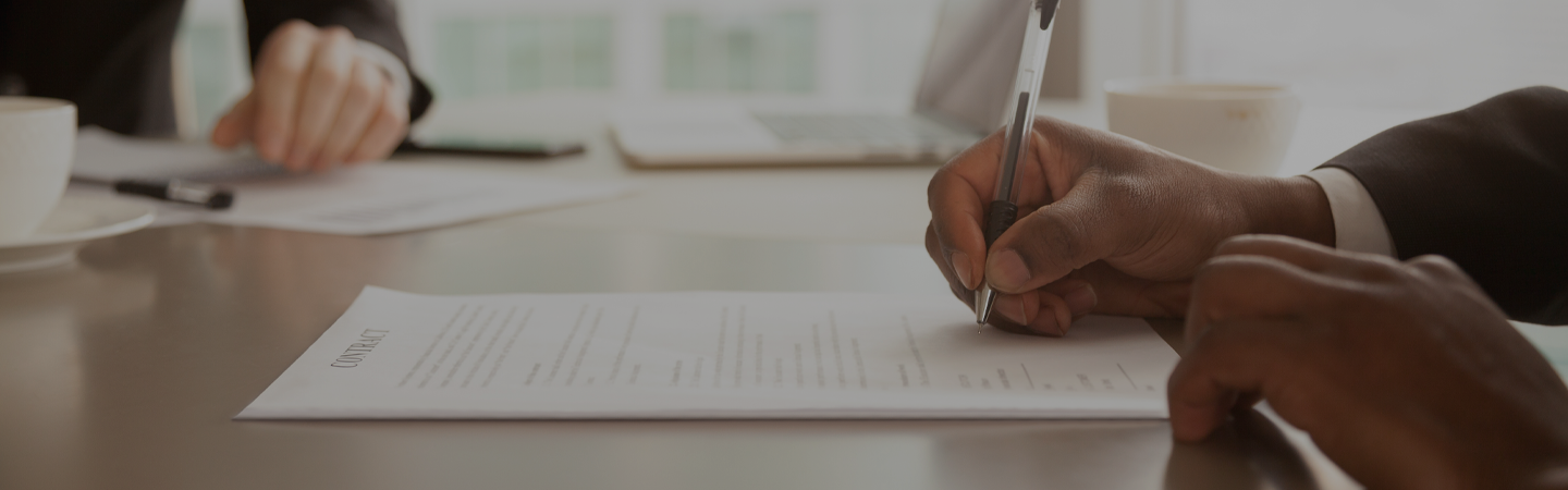 business man sitting at an office deck, holding a pen to sign contract papers.