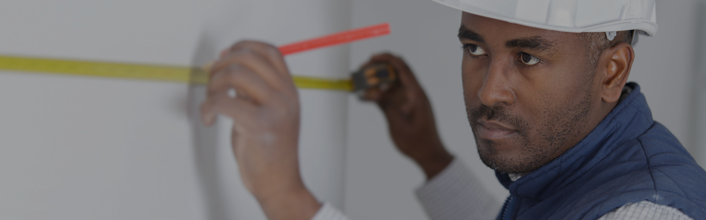 male tradesman using a yellow tape measure to mark up white plastered wall on site.