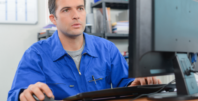 A tradesman using a work computer sat down at a deck, wearing blue construction clothing.